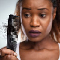 Femme regardant des cheveux cassés dans un peigne après le démêlage, illustrant la casse des cheveux crépus.