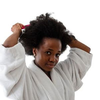 Femme en peignoir démêlant ses cheveux crépus dans le cadre d'une routine capillaire naturelle Kaylabé.